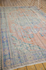 Distressed Oushak rug corner showing worn apricot, blue, and ivory floral patterns.