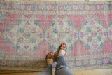 Distressed Oushak rug runner: faded red rose, beige field, ocean green, pink Rococo motifs.