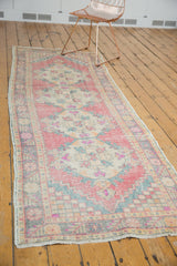Distressed Oushak runner corner displaying faded red rose, beige, and checkered spandrel.