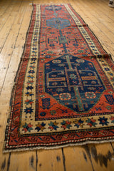 Antique Northwest Persian runner with navy blue medallion, cherry red floral field, and visible wear.