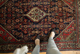 Feet on vintage Engelas rug, highlighting navy Herati field and brick red serrated border.