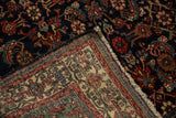 Corner of vintage Engelas rug revealing navy Herati design, red accents, and light foundation with fringe.
