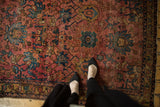 Antique Lilihan rug with feet, highlighting even wear and raspberry, gold, blue palmette motifs.