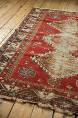 Tattered end, geometric pawn motif border, and worn red field of antique Caucasian rug.