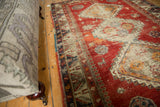 Antique Caucasian rug: geometric pawn border, cherry red field with scattered animal motifs and storied wear.