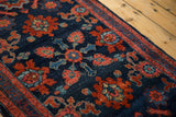 Corner of an antique Persian Lilihan rug, intricate floral pattern on navy field, showing wear.