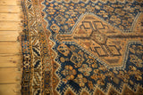 Vintage Kamseh rug's time-softened navy and copper hues, geometric border, and frayed end.