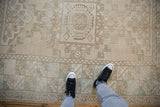 Feet on vintage distressed Oushak rug, showing wide geometric border and muted beige and mint tones.
