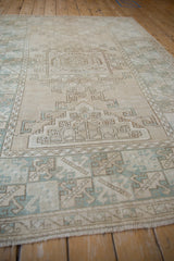 Distressed Oushak rug's geometric medallion and four leaf border detail in beige and dusty mint green.