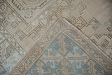 Distressed Oushak rug's folded corner, showing beige geometric patterns and dusty blue accents.