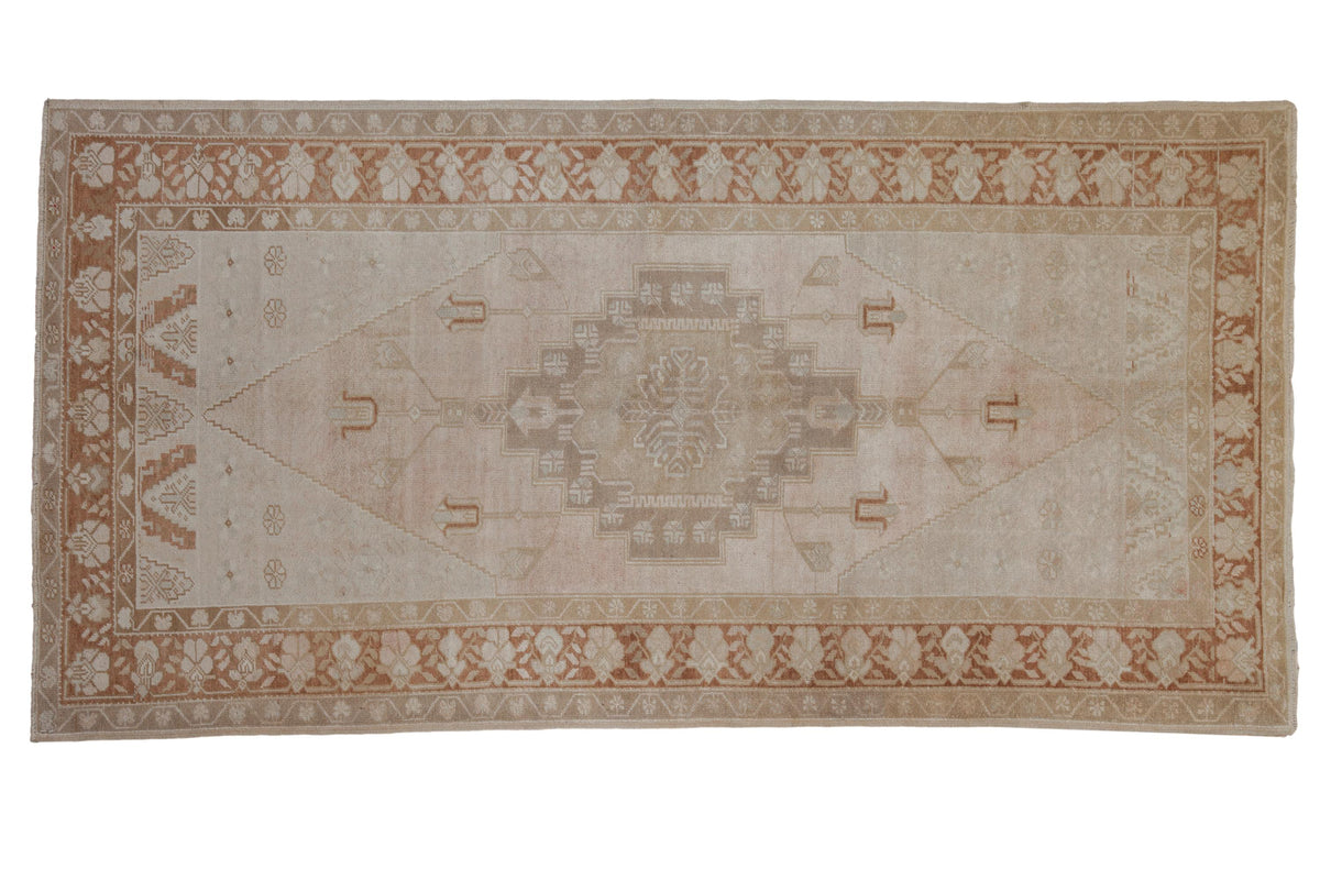 Vintage distressed Oushak rug with a stepped diamond medallion in a palette of pale blush, copper, and beige.