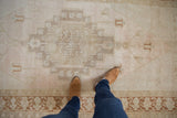 Low pile and even wear of a distressed Oushak rug with soft blush and beige coloration.