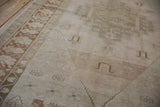 Angled view of the copper bronze floral border beside the pale blush field of a distressed Oushak rug.
