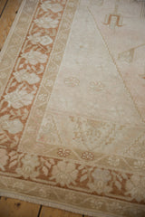 Distressed Oushak rug corner with a copper-bronze floral border and a low-pile beige field.