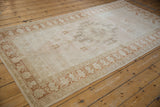 Angled perspective of a vintage distressed Oushak rug showing its soft blush, ivory, and copper bronze palette.
