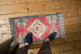 Decorative distressed Oushak mat with worn cherry red pile, ivory stepped medallion, and aqua geometric border.