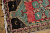 Distressed Oushak rug corner showing soft fringe, geometric border, and muted aqua, rose blush, charcoal.