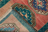 Distressed texture of a folded Oushak rug with blush, aqua, and bronze hues.