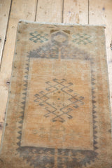 Angled view of distressed vintage Oushak rug mat, showcasing faded beige and mallard green patterns.