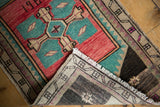 Distressed Oushak rug mat folded corner, showing low pile, fringe, and beige geometric border.