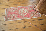 Distressed blush and ivory Oushak rug pile, highlighting worn texture and geometric patterns.
