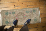 Distressed Oushak rug's low pile, beige field with aqua green and pink motifs.