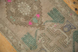 Beige, aqua green, and bright pink plant motifs on distressed low pile vintage Oushak rug.