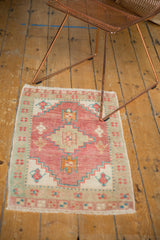 Distressed Oushak rug corner, revealing soft pink and seafoam geometric patterns and fringe.