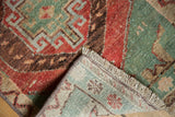Distressed vintage Oushak rug corner, showing worn red, green, brown geometric pattern and fringe.