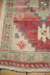 Distressed Oushak rug corner, showing faded cochineal, seafoam geometric patterns, and fringe.