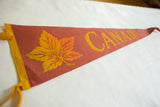 Close-up of vintage Canada felt pennant showing burnt orange texture, gold maple leaf, and CANADA lettering.