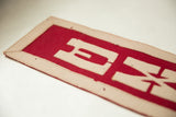 Textured cream felt appliqué on red vintage Exeter banner, with age-softened details.