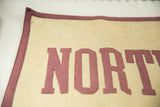 Detail of vintage felt banner showing stitched maroon letters, cream background, subtle patina.