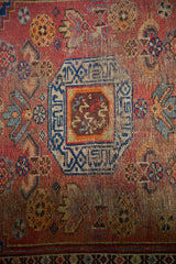 Antique Kurdish rug detail: stepped navy medallion, madder red field, and visible pile wear.
