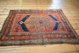 Detailed view of antique Kurdish rug corner showing tattered end, worn pile, and geometric border.