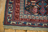 Corner of hand knotted Antique Kuba rug with original macrame ends, geometric borders in blue, red, and ivory.
