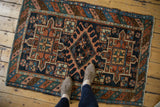 Corner of an antique Persian Karaja rug featuring a geometric medallion, floral motifs, and secured polychromatic selvage.