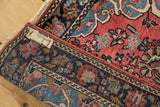 Rolled vintage Mohajeran Sarouk rug showing dusty rose field, floral motifs, navy border, and tag.