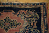 Antique Senneh rug corner with indigo scrolling vinery, blush field, geometric border, and even wear.