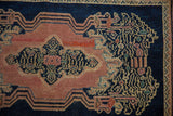 Visible reweave on the blush dusty rose field of the antique Senneh rug, with navy scrolling vinery.