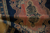 Folded antique Senneh rug with blush dusty rose field, indigo border, scrolling vinery, and faint foundation.