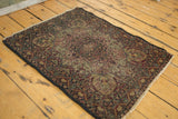 Detail of antique Kerman rug, highlighting its mostly even wear, worn end, and ornate cochineal red floral field.