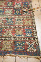 Antique Caucasian rug's tattered end, showing geometric palmettes and wave borders.