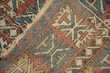 Close-up of antique Caucasian rug with geometric palmette motif, visible foundation, and tattered edges.
