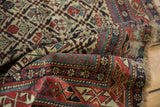 Folded antique Marsali Caucasian rug with rich red borders, intricate geometric motifs, and fringe.