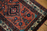 Corner detail of a vintage Persian rug showing the floral and wave motif borders against a rusty red field.