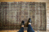 Antique Kerman rug corner with hard wear, threadbare vinery pattern, and tattered fringe.