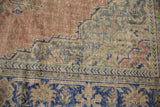 Distressed Oushak rug section with pale blush, cobalt blue vinery, and visible pile wear.