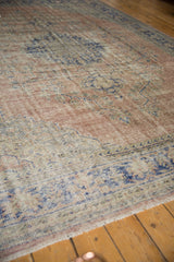 Distressed Oushak carpet's low pile texture with pale blush and muted cobalt blue patterns.