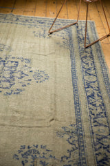 Distressed pale celadon Oushak rug showing worn pile and faded cobalt blue border.